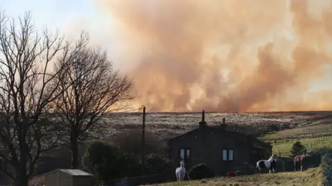 Rod Iveson Smoke hovering on horizon near house on moorland