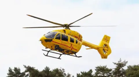 Yellow East of England Air Ambulance mid flight