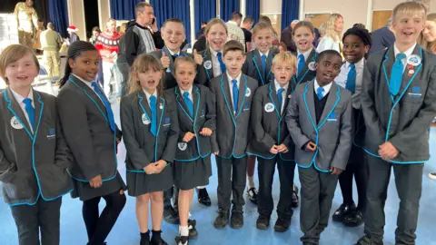 BBC School children gathered in a group and smiling at the camera at the box packing event.