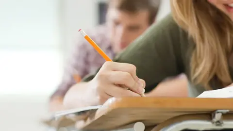 Students work in jotters on wooden desks in a classroom.