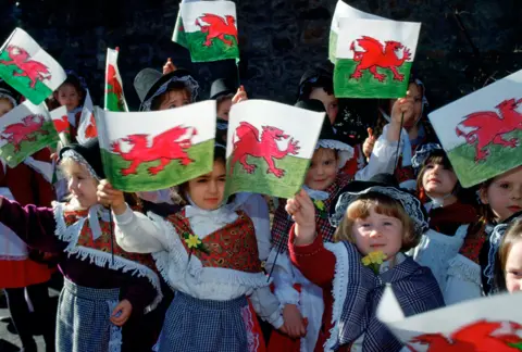 Tim Graham Photo Library/Getty Images Children Gather In Wales To Meet Prince William On St David's Day. They Are Dressed In Traditional Welsh Costumes And Waving Flags.