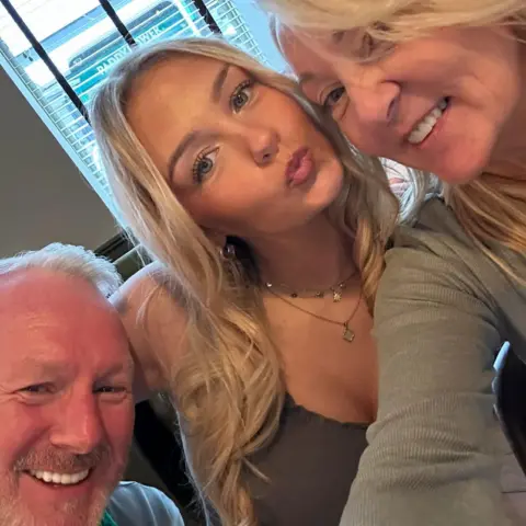 Diane Lees Three people pose for a selfie - a man with short white hair smiles, a woman with long blonde hair pouts in the middle and another woman with blonde hair smiles