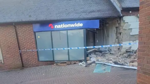 Laura Barford A damaged Nationwide building society, with debris on the ground, blue and white police tape across the front. A window has been partially pulled out. 