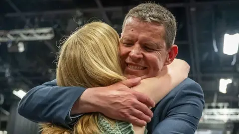 Plaid Cymru's Rhun ap Iorweth embraces his wife after winning his seat