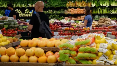 Getty Images Fruit and vegetables stacked as customers browse a grocery shop. 