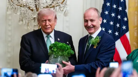 EPA/Jim Lo Donald Trump (left) beside Micheál Martin who is presenting him a shamrock bowl. Both wearing dark suits and green ties. Martin has a shamrock on his lapel. Both have grey hair.