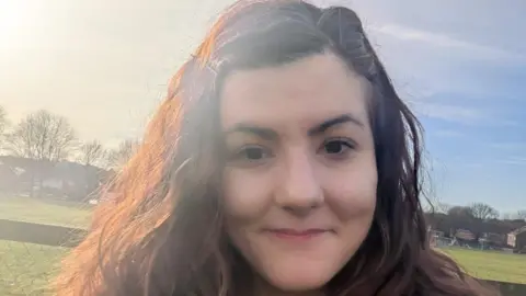 Contributed Samantha Morgan looking at the camera, she has long dark hair. In the background is a field with trees.
