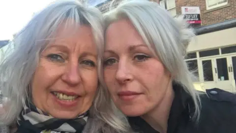 Supplied Dr Sue Robson smiling next to her daughter Tina Robson in a selfie. They both have straight platinum blonde hair. Sue is wearing a scarf and Tina a black jacket.