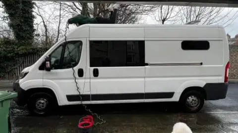 White van with elongated black windows on road