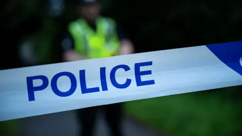 A stock image of police cordon. A police officer is blurry in the background. 