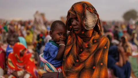 Getty Images A woman wrapped in orange African print holds a young child. 