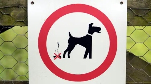 A sign detering people from dog fouling tied to a fence in a field