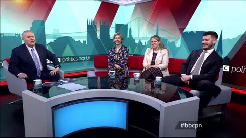 Tim and the three politicians sit on a curved sofa around a curved desk in the BBC red branded colours. Politics north is on a strap-line across the set at the back.