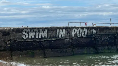 Joshua Askew A large sign saying swimming pool in white has had certain letters painted out to read 'swim in poo'.