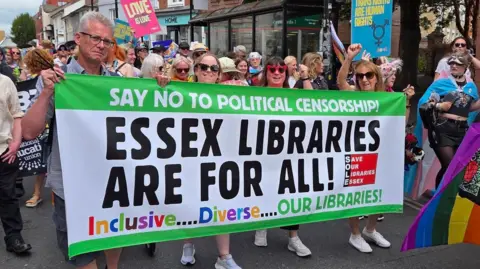 Library campaigners join a Pride march in Chelmsford. They are holding a large green and white banner that says: "Say no to political censorship. Essex libraries are for all. Inclusive, diverse - our libraries."