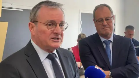 Matthieu Guillot/AFP/Getty Images Jacques Billant speaks into a microphone as a man behind him looks on