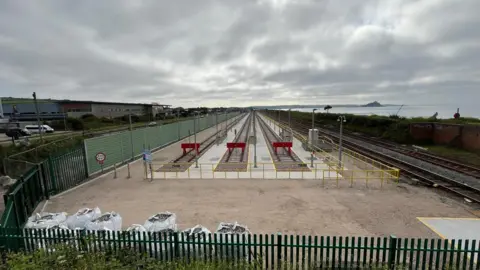 Three railway tracks at the centre of the site. There is a green fence surrounding the tracks and there are three barriers at the end of each track.