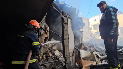 Firefighter and man stand amidst the rubble in Burj Al-Barajneh, Beirut