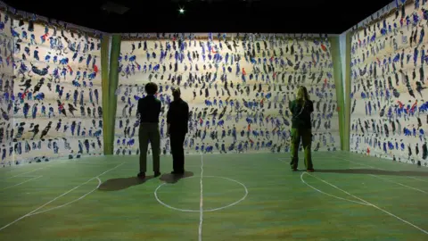 Michael Pollard Three people stand in front of a digital screen depicting LS Lowry's painting.