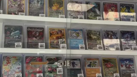 Trove UK A glass display cabinet with rows of Pokemon cards inside