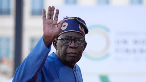 AFP Nigeria President Bola Tinubu, wearing a blue gown and hat, waves as he arrives for the closing session of the New Global Financial Pact Summit, on June 23, 2023 in Paris