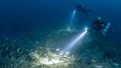 Rick Ayrton SS Nantes from above with the dive team. Lots of fish around the wreck and the divers have torches.