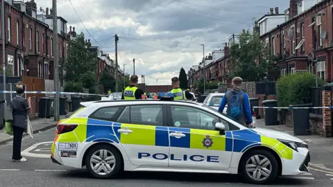 A police car blocks the entrance to a residential terraced street.