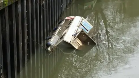 A sunken boat in a canal in the Bath and North East Somerset Council area. It is partially submerged.