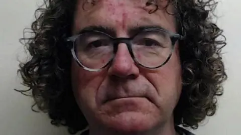 A mugshot of Roderick Bryce-Hagain, who has shoulder-length dark hair.