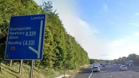 Blue and white motorway sign on left with motorway and traffic on the right