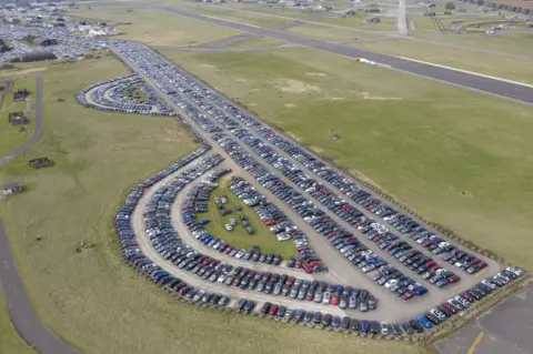 Chris Gorman / Big Ladder Aerial view of cars being stored on airport runways