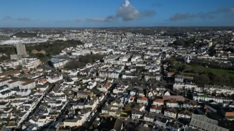 Ariel shot of South St Helier. Jersey. There are rows of houses and buildings below. The photo was taken on a cloudy day.