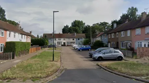 A cul-de-sac with residential houses and cars parked outside. The sky is cloudy.