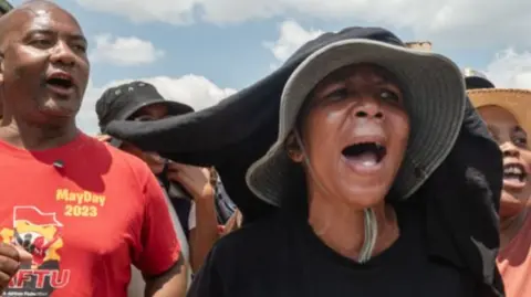 A man in a red shirt and a woman wearing a sunhat and black shirt chant at a demonstration outside the mine.