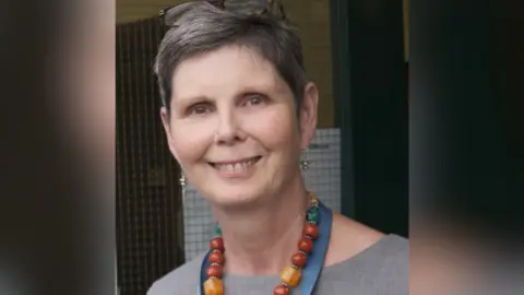 Citizens Advice Angela Kerr is seen from her shoulders up smiling at the camera. She is wearing a chunky necklace and has short hair.