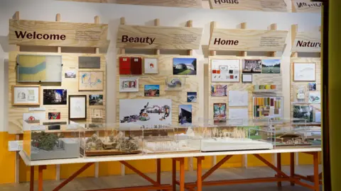Wall and glass cabinet displays at the Maggie's Exhibition at the V&A Dundee. The cabinets have models of various Maggie's Centre buildings and headings on the wall display say "Welcome", "Beauty", "Home" and "Nature".