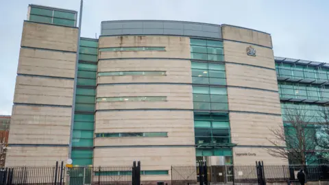 PA Media Outside Laganside Courts in Belfast. It is a cream building with a lot of windows and black buildings at the front.