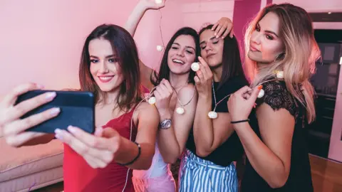 Getty Images Young women posing for a photo on a phone