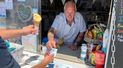 Guernsey Dairy Gary De Carteret handing an ice cream to a customer at Pembroke Beach Kiosk