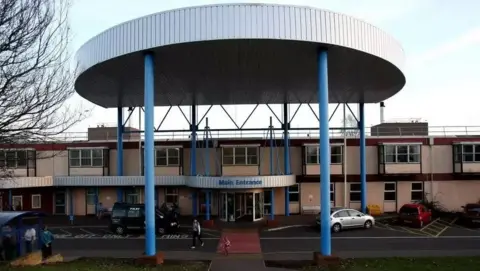 Exterior of current Hinchingbrooke Hospital showing wide overhanging facade and signage