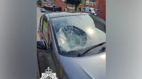 A parked grey car with a damaged windscreen after Cook had thrown his dog at it