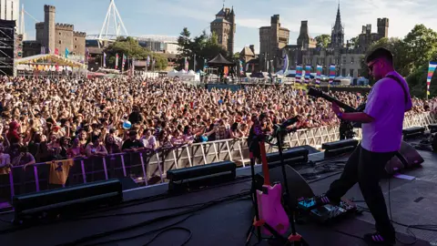 Menter Caerdydd Stage view looking out towards a packed crowd at Cardiff Castle with part of the city skyline in view, including the Principality Stadium