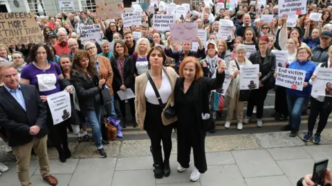 PA Media Two women, backed by a crowd holding placards and signs, protest against the sentence of a man convicted for an assault on Natasha O'Brien. 