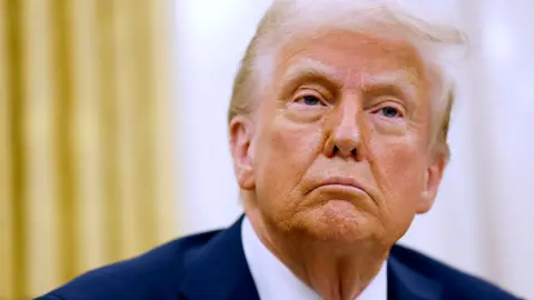 Getty Images A close up headshot of US President Donald Trump looking on as reporters ask questions, after he signed a series of executive orders in the Oval Office of the White House on 23 January