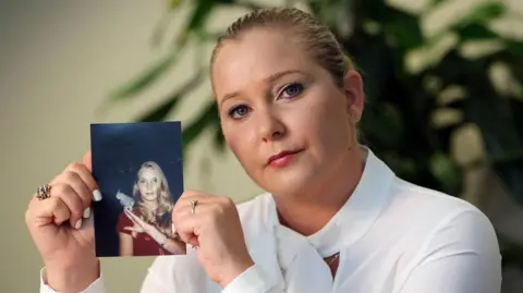 Getty Images Virginia Giuffre pictured in November 2022 looking into the camera and holding up a photo of herself as a teenager.