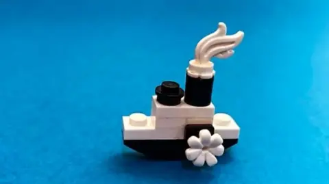 A small lego steam boat using black and white bricks is on a blue background