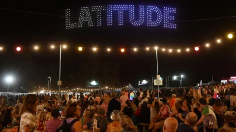 Jim Dyson/Getty Images Large crowds - both seated and standing - admire a large drone display which spells Latitude in the dark sky.