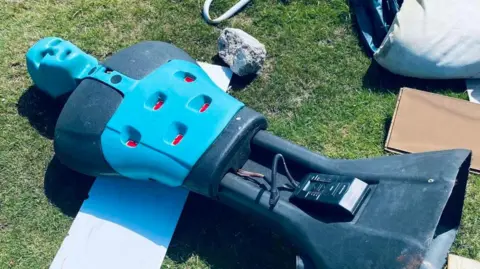 A blue and black plastic mannequin has been left on the grass among other waste items.