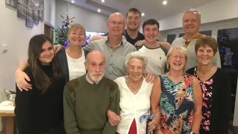 Family handout Four women and five men, of various ages, pose with Marjorie in a home, smiling at the camera 