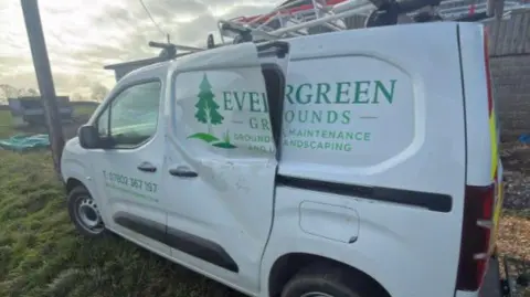 Jack Roberts A white van parked up on grass with green letters saying Evergreen Grounds. The door is badly dented and partially hanging off. 